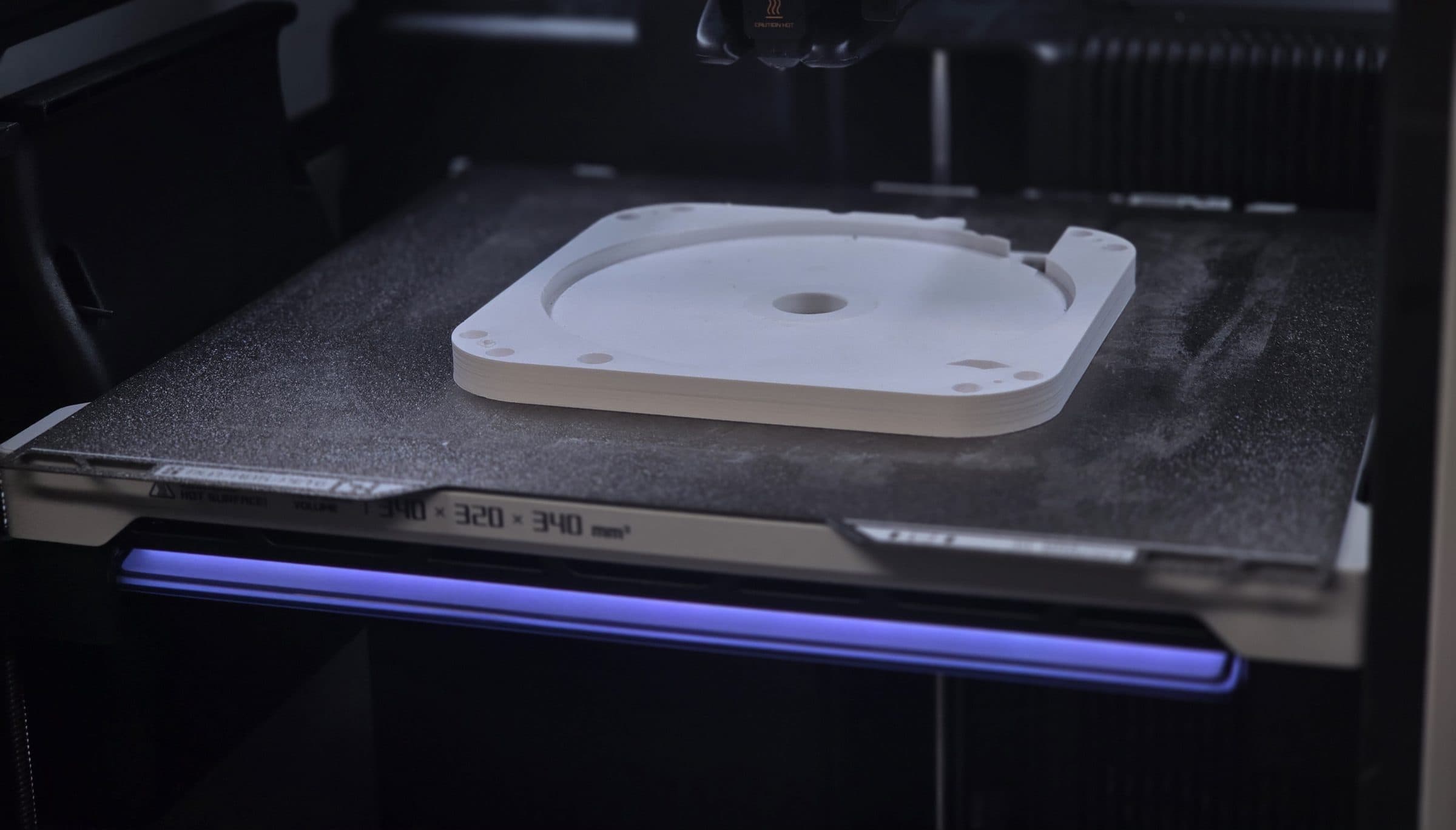 An FDM 3D printer mid-print, a white part on the build plate